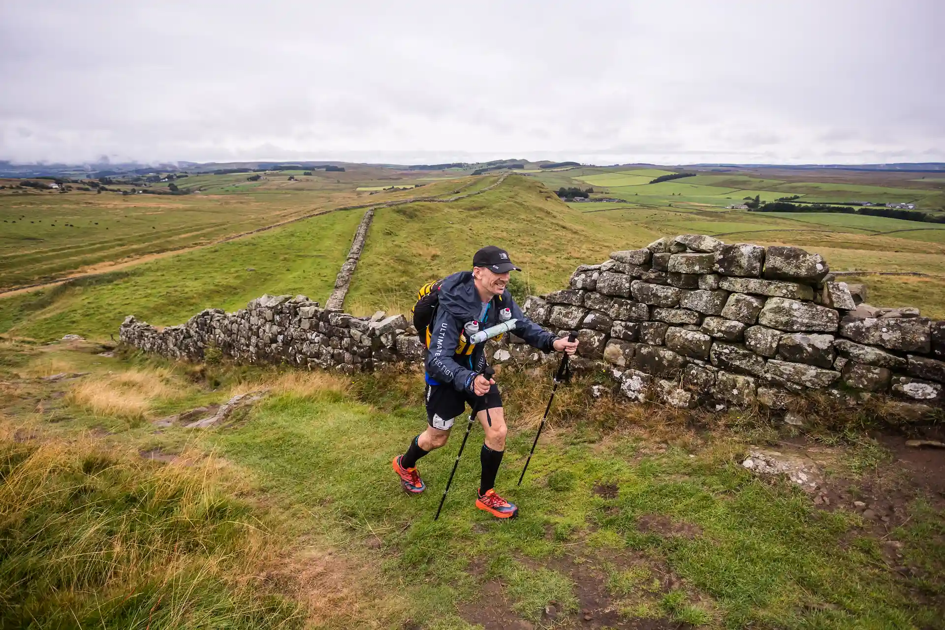 PFM Coaching head coach Steve using trekking poles during an ultra marathon trail race along a scenic stone wall.