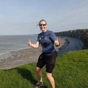Smiling runner giving two thumbs up on a grassy cliff overlooking the sea
