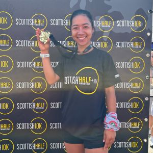 Smiling runner holding a finisher's medal in front of a Scottish Half + 10K backdrop