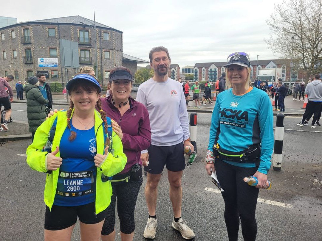 5 Reasons to Hire a Running Coach for Your Next Running Challenge Four smiling runners posing together on a street before a running event, with one woman giving two thumbs up