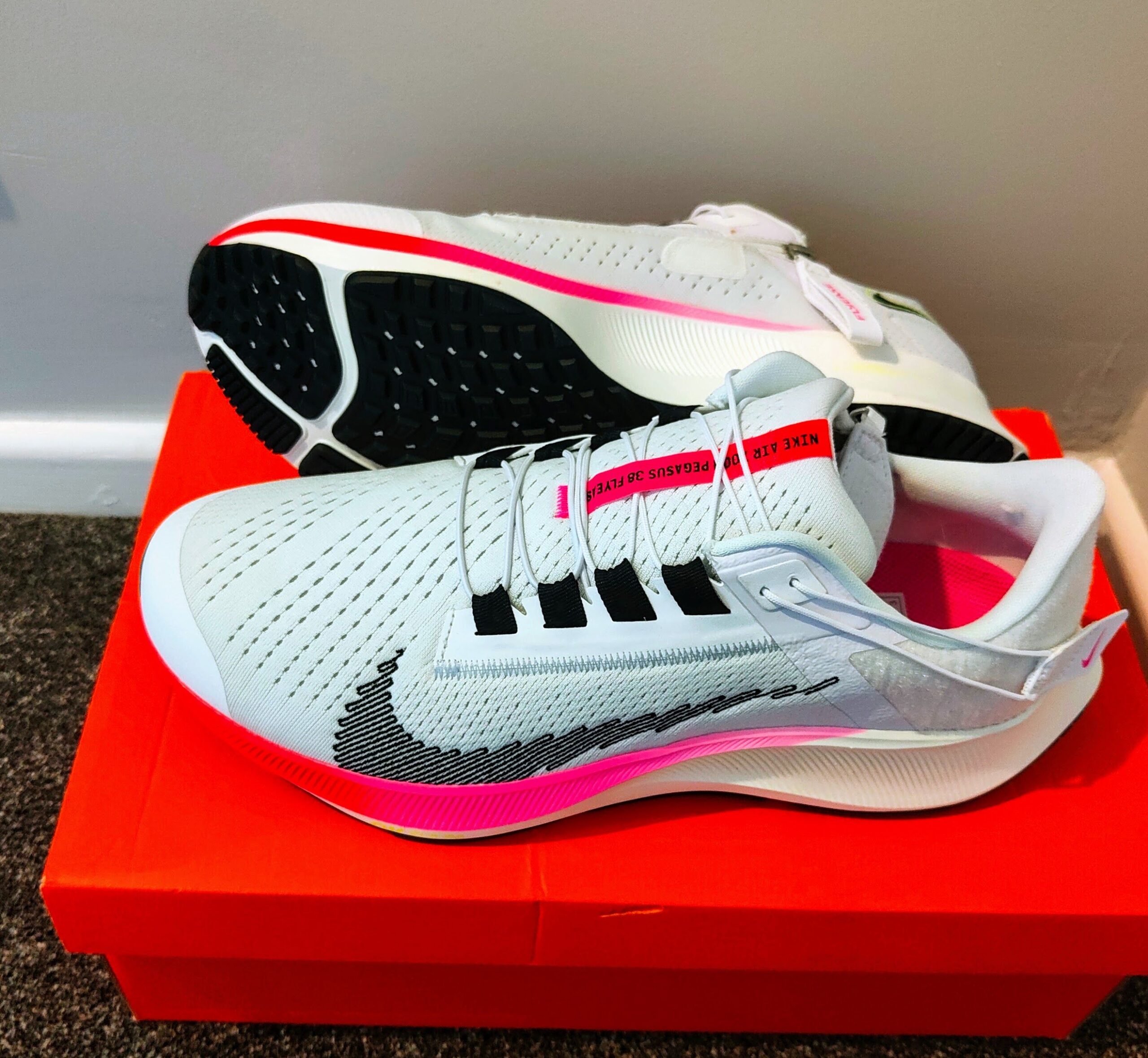 White Nike Air Zoom Pegasus 38 FlyEase running trainers with pink accents resting on an orange shoe box